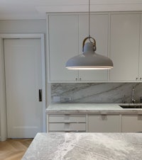 a kitchen with white cabinets and marble counter tops